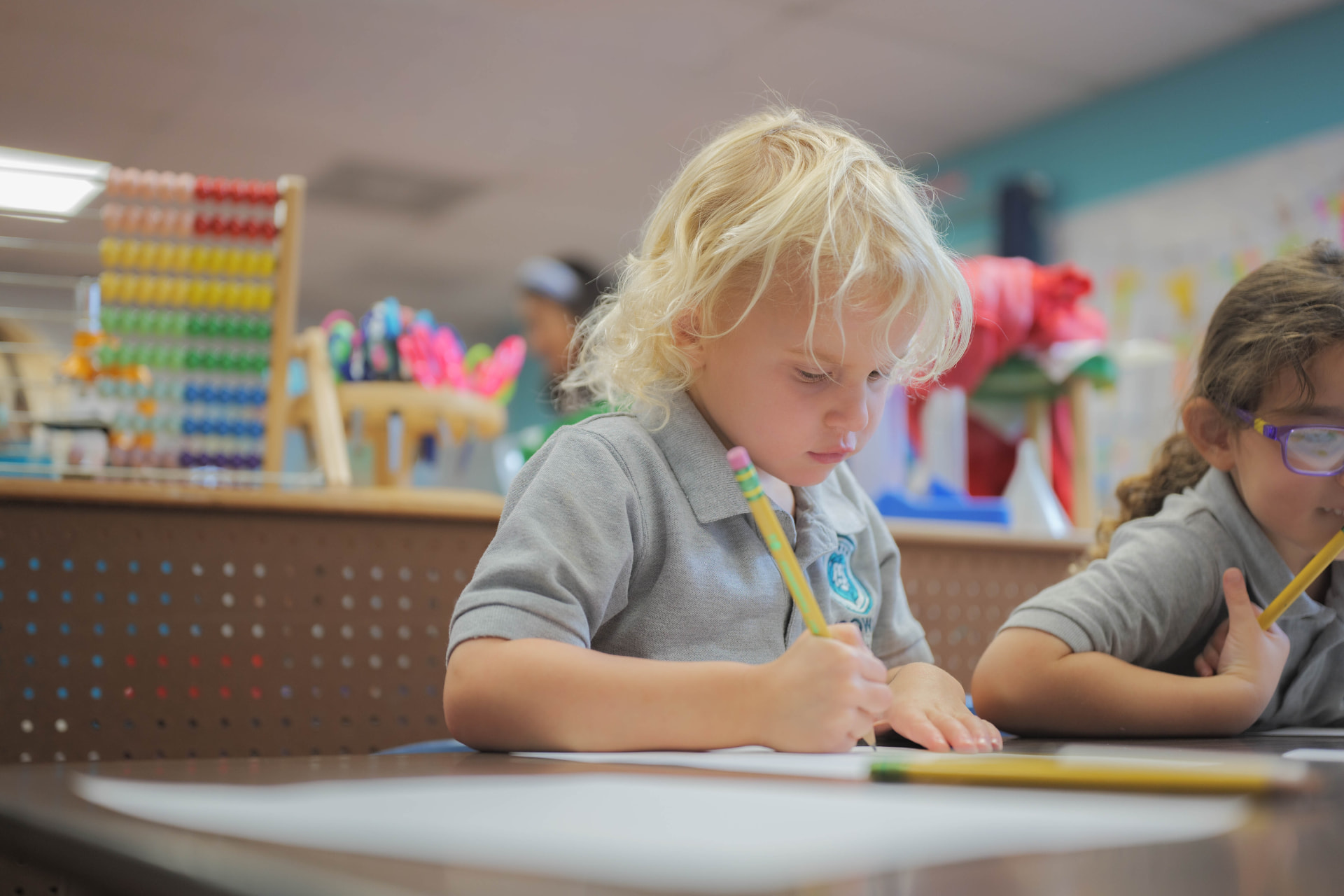 Preschooler practicing writing with a pencil at a classroom table
