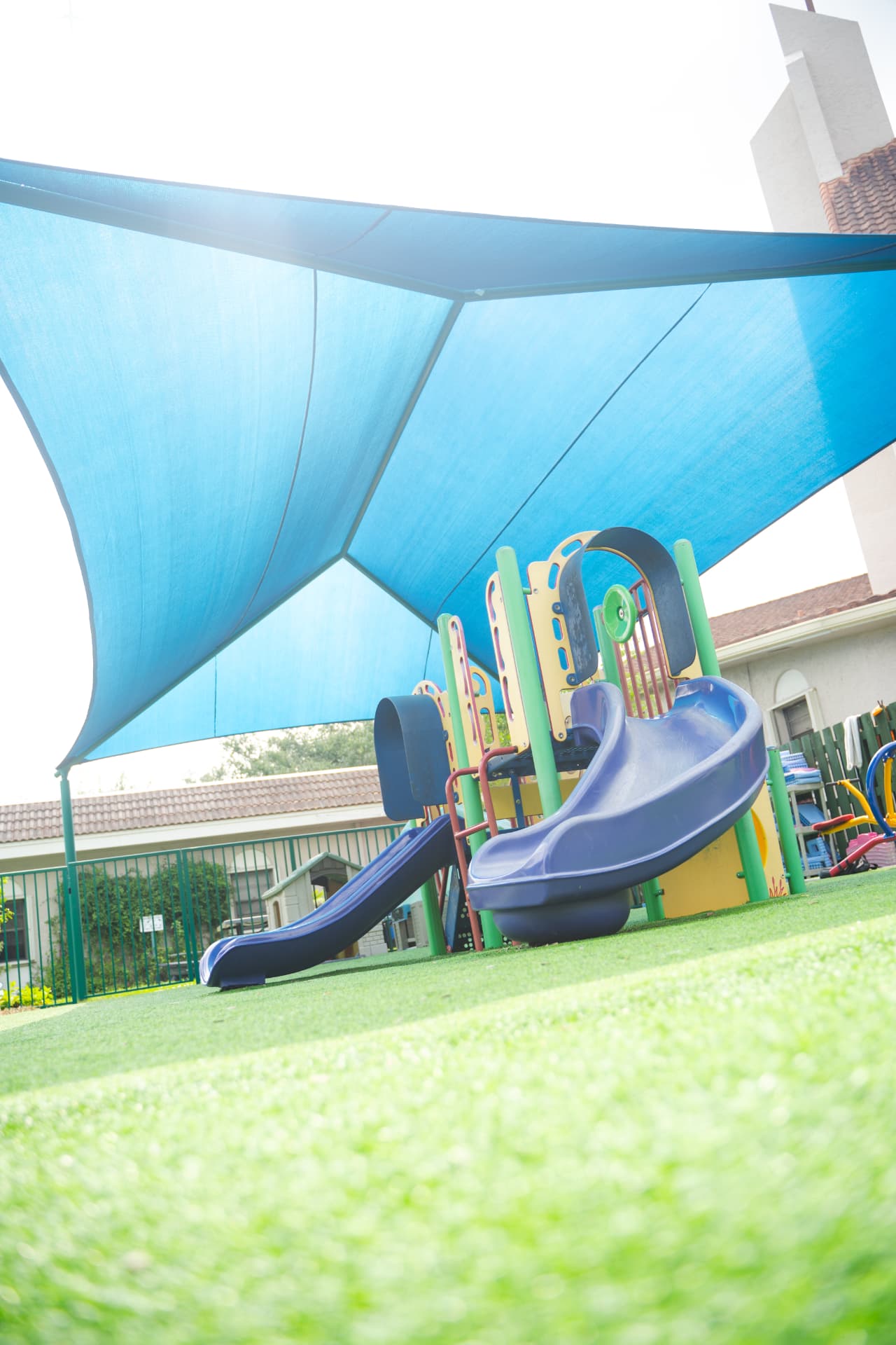 Shaded preschool playground with slides and turf surfacing under a large blue sun canopy