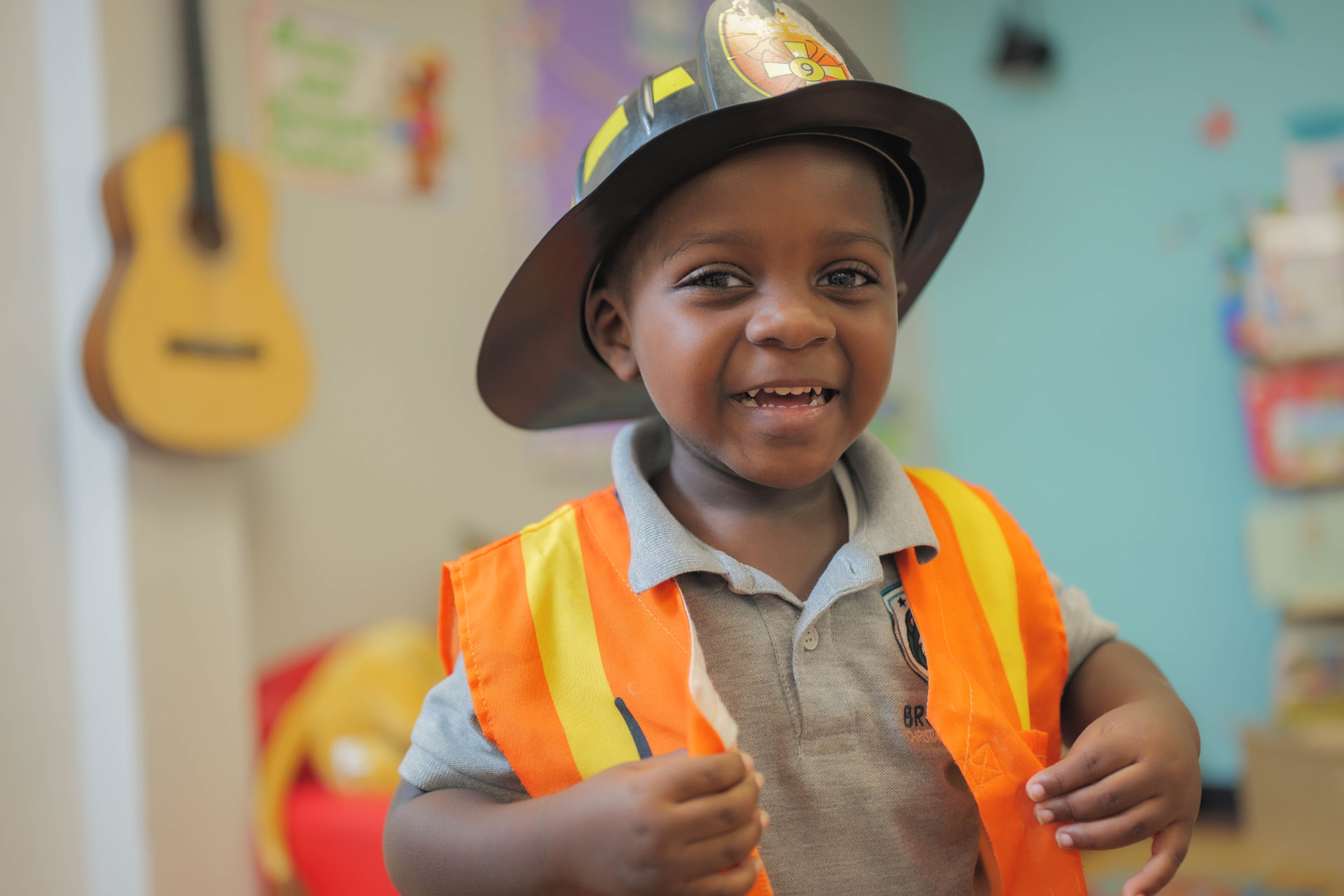Smiling preschool boy wearing a firefighter hat and safety vest during dress-up play