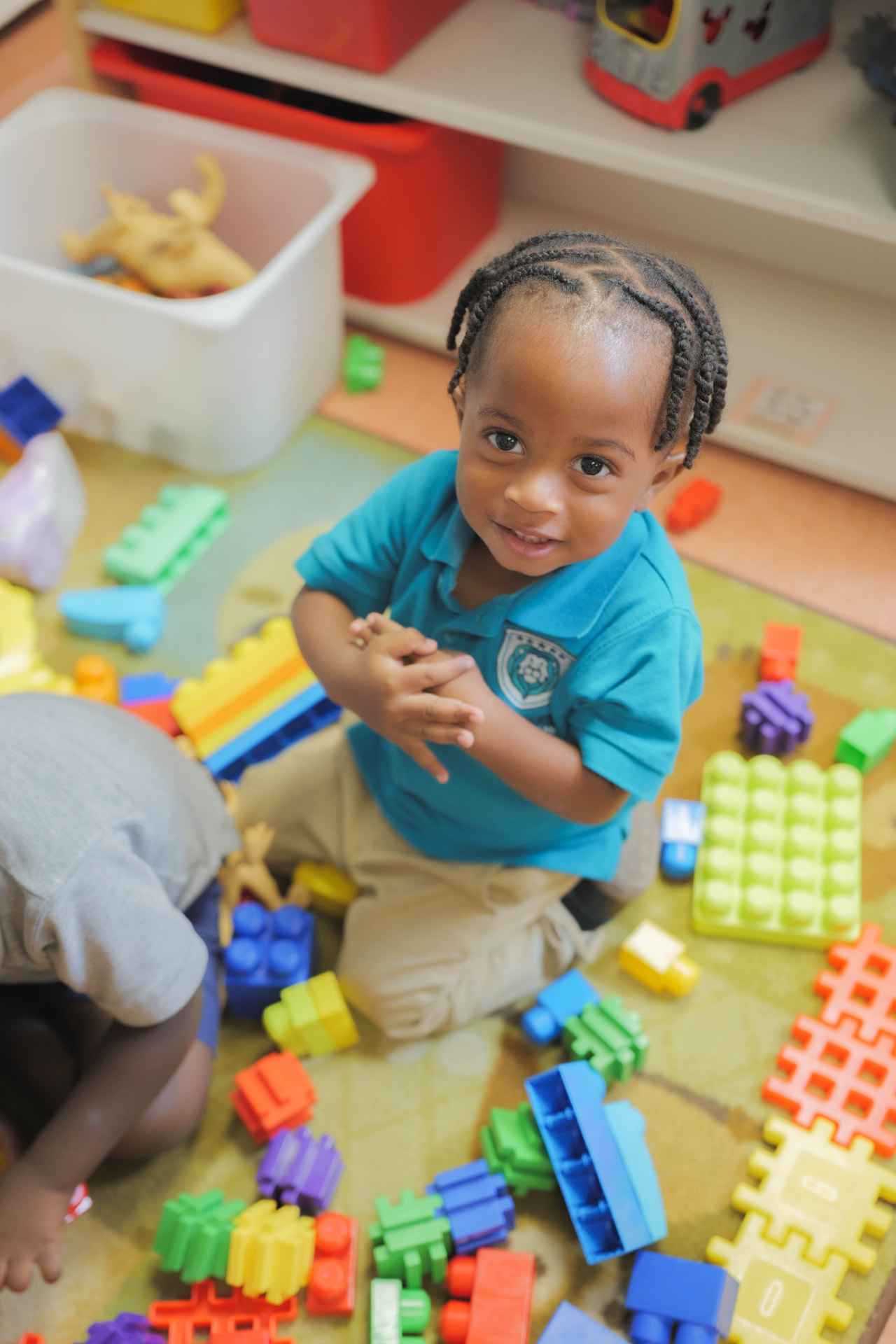 Smiling toddler playing with colorful building blocks on the classroom floor