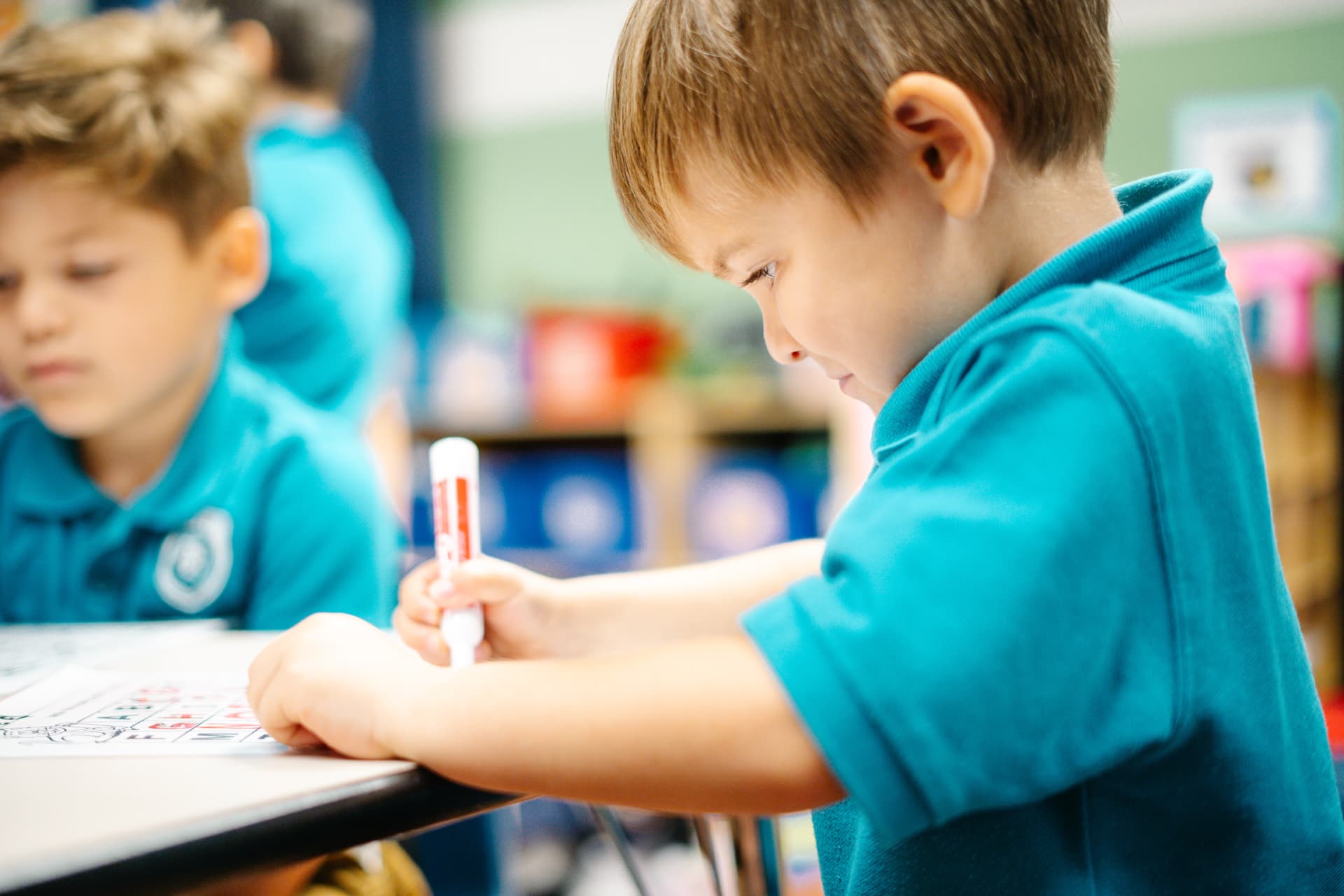 Young student focused on a classroom writing activity with a marker