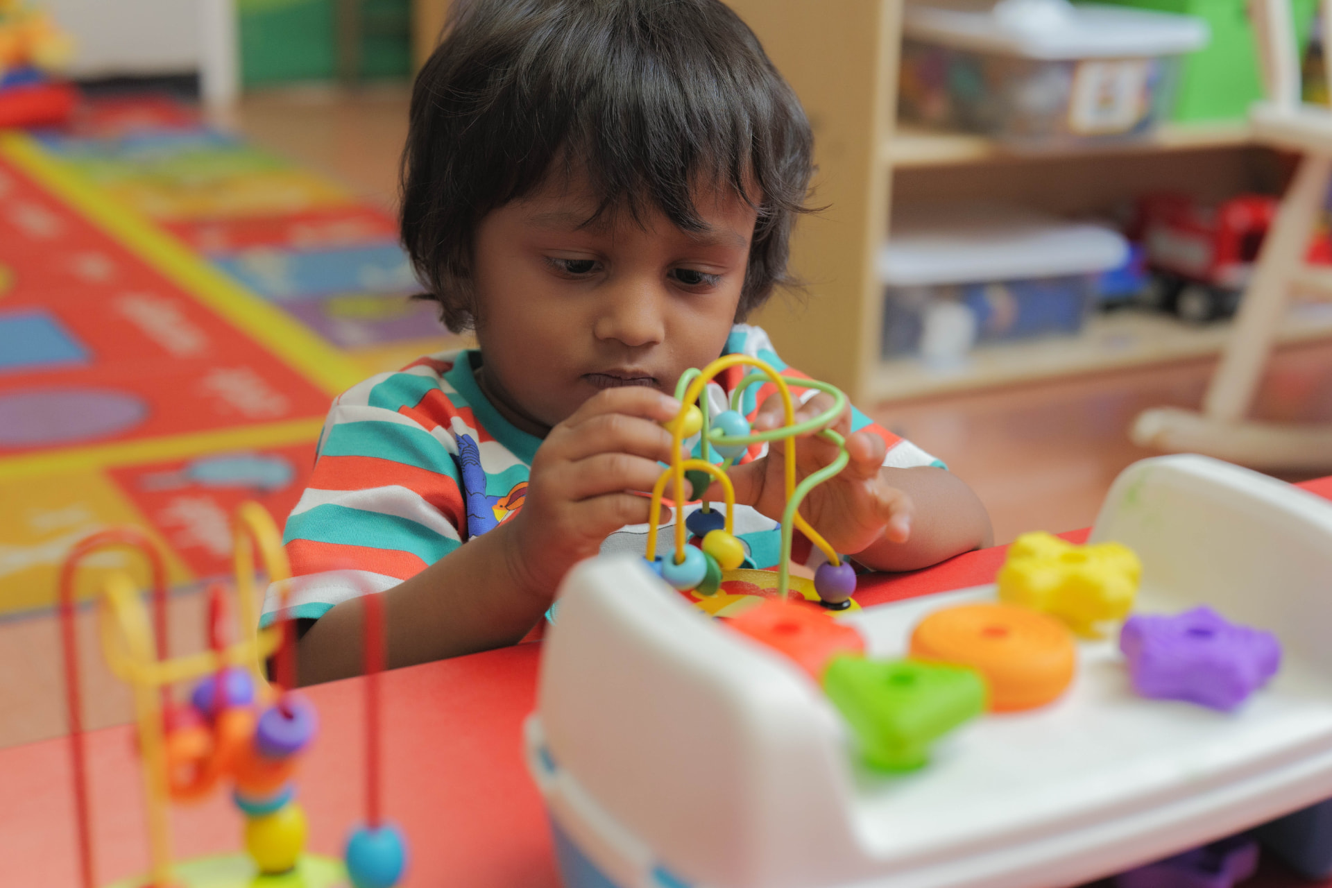Toddler exploring a colorful bead maze toy at a classroom table