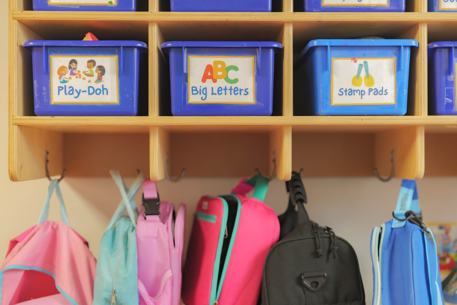 Preschool classroom cubbies with labeled learning-center bins and children's backpacks set up with hands-on learning centers